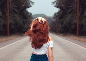 Red-haired woman in jean shorts walking down a forest road, showcasing style and freedom.