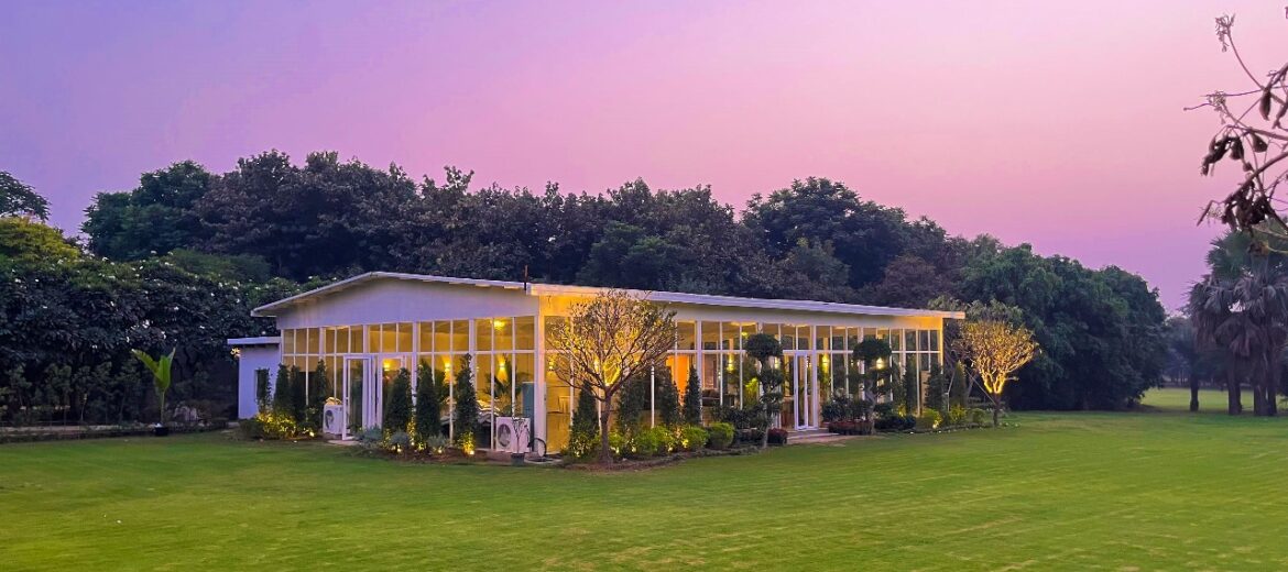 Modern glass-house banquet hall at Botanix Nature Resort, Gurgaon, with floor-to-ceiling windows blending indoor event space with lush outdoor greenery